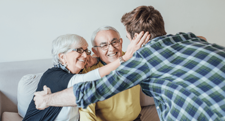 a young man leaning in to hug a smiling elderly couple