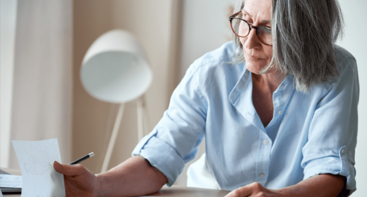 older woman sitting at a table and looking through her bills