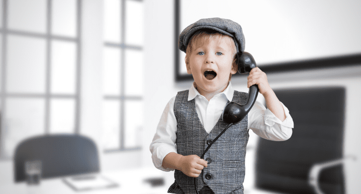 Young child in business attire, holding a phone to his ear, with a surprised look on his face